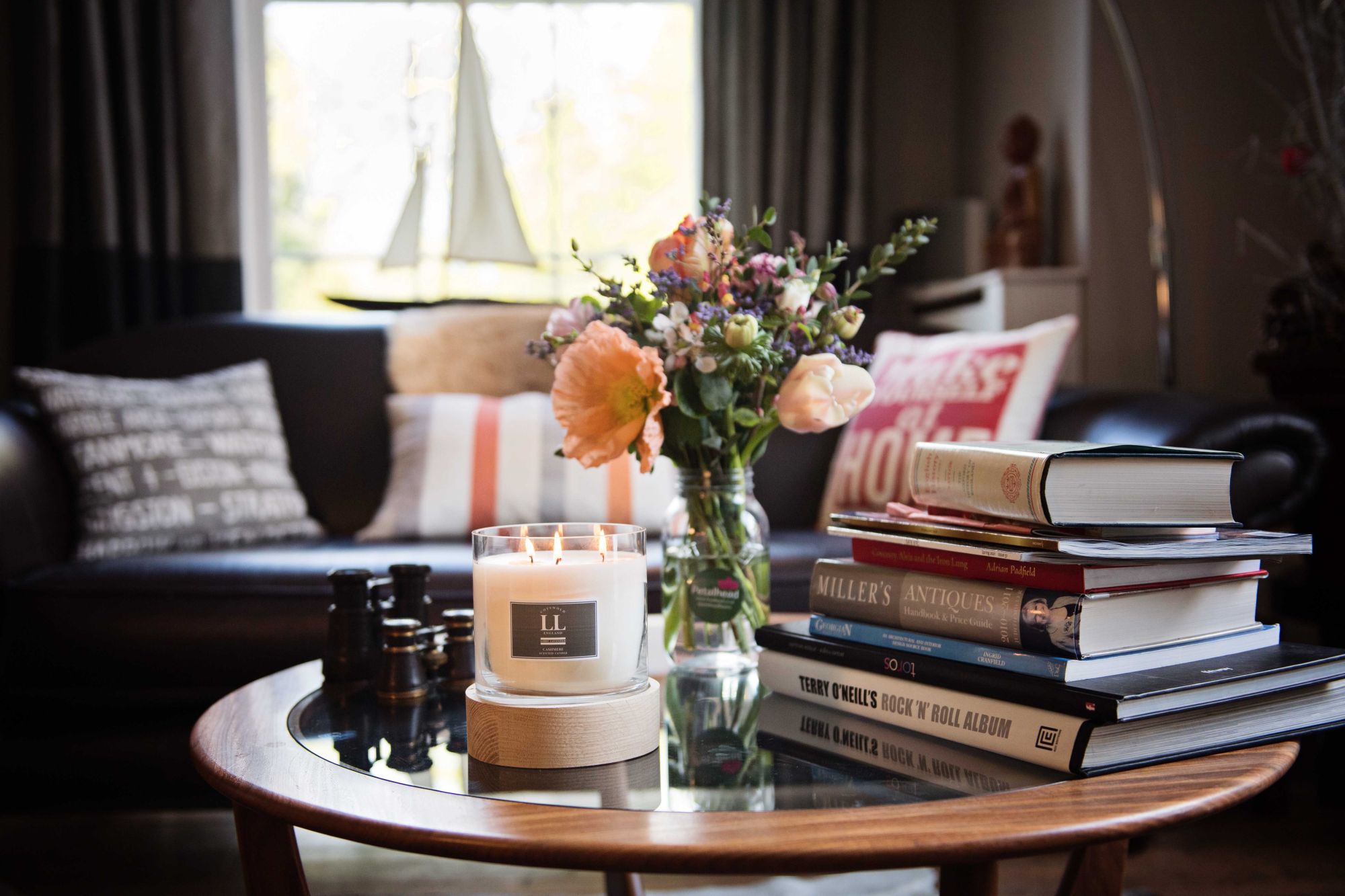 Lifestyle image of candle lit on a wooden and glass table surrounded by inspirational books and ornaments. 