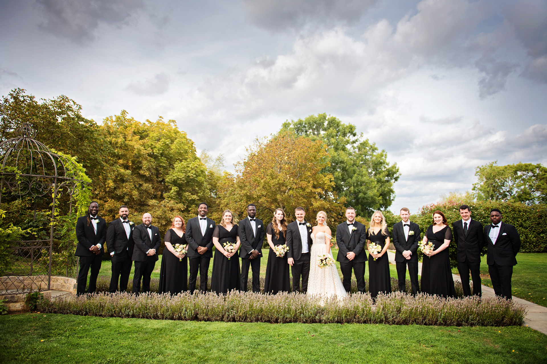 Bridal party pose for their photo along a lavender pathway with the bride and groom, autumnal tree's behind them.