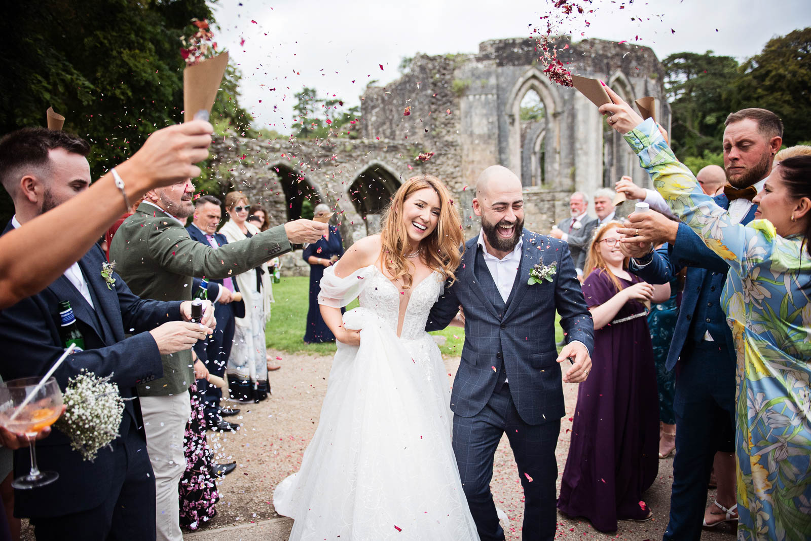 Bride and groom walking through a people archway with their wedding guests throwing confetti at them.
