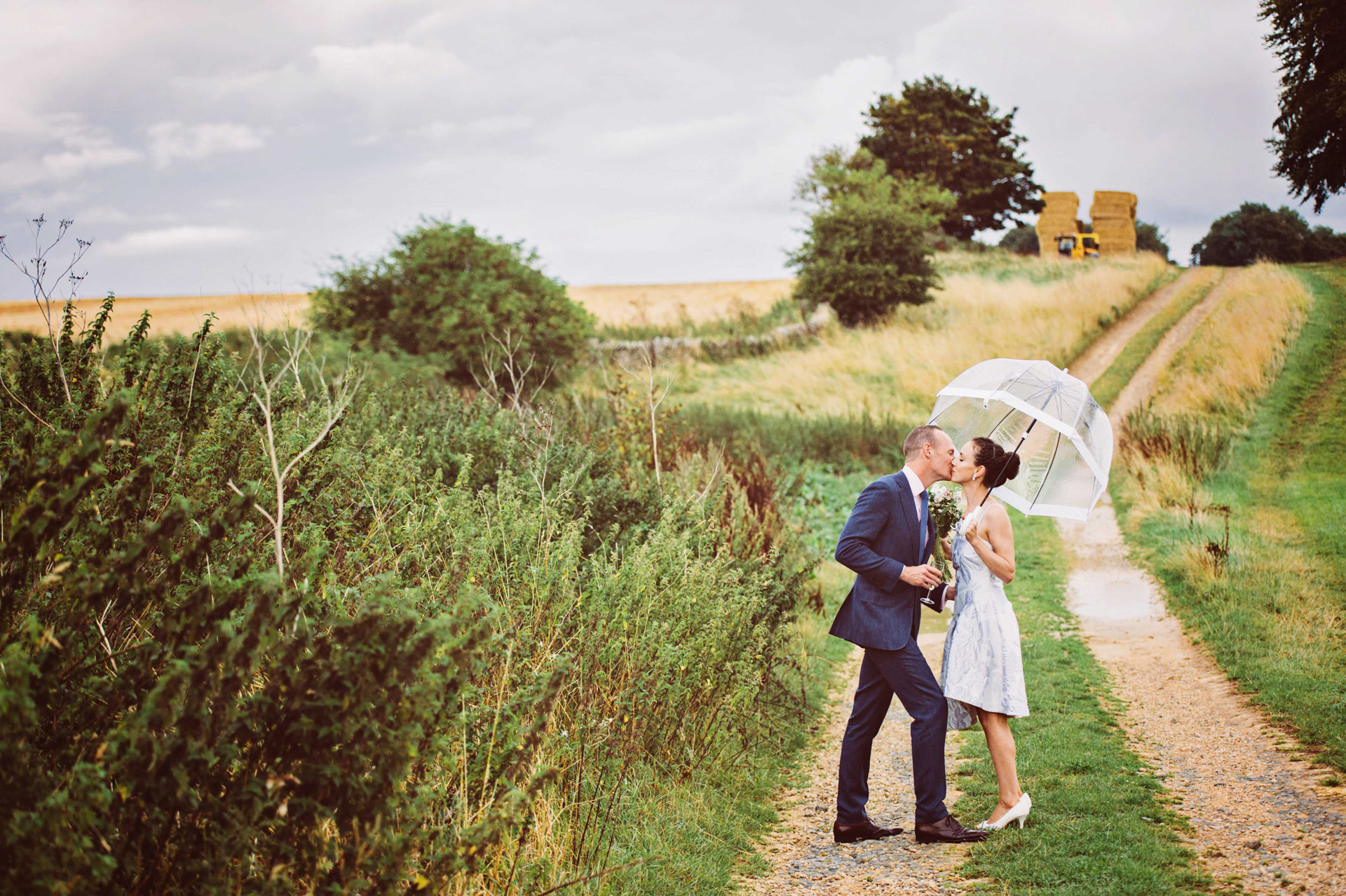 Cotswold wedding, bride and groom kiss, rainy wedding, Stone Barn wedding, knee length wedding dress