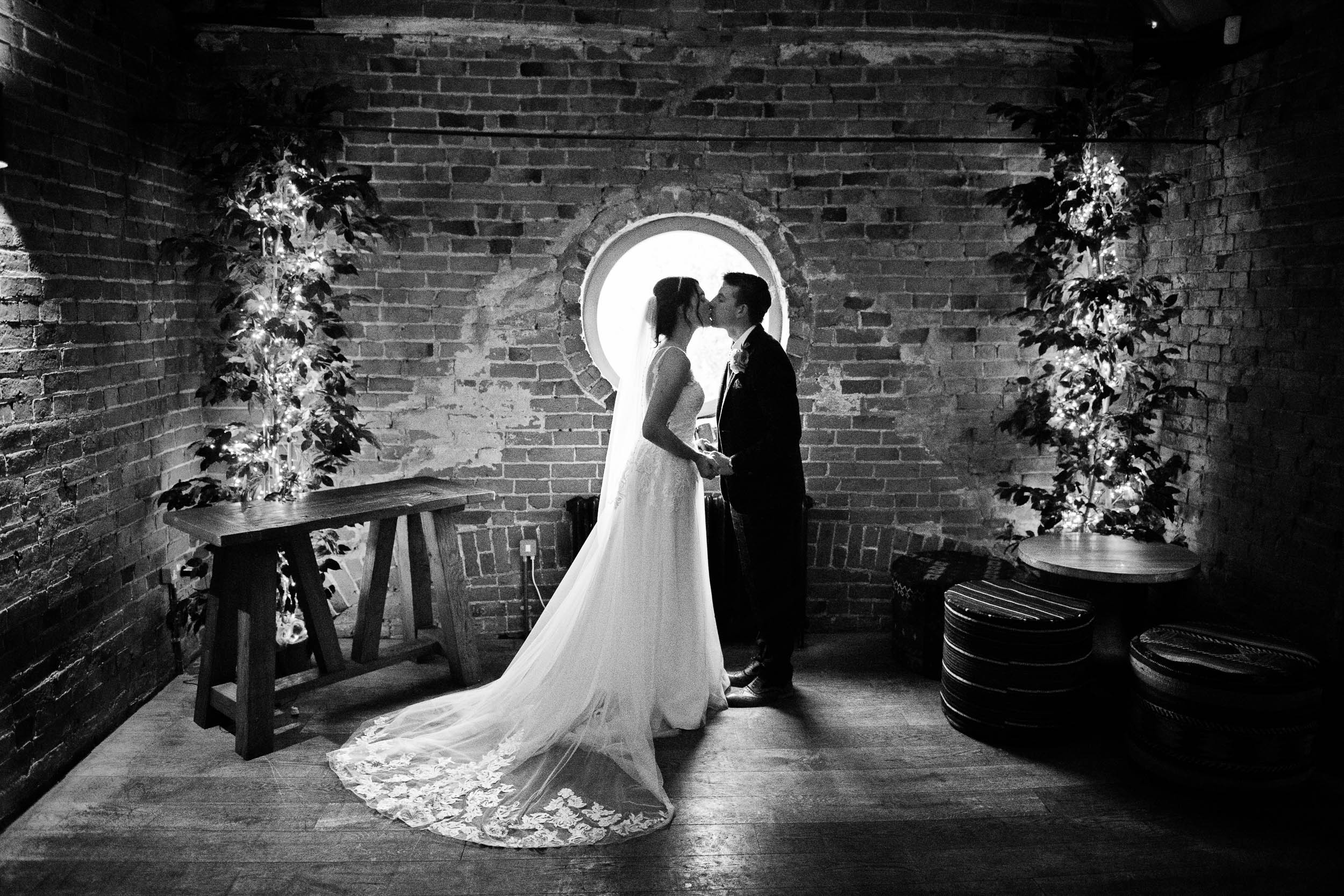 B&W image of bride and groom kissing in front of a window.  