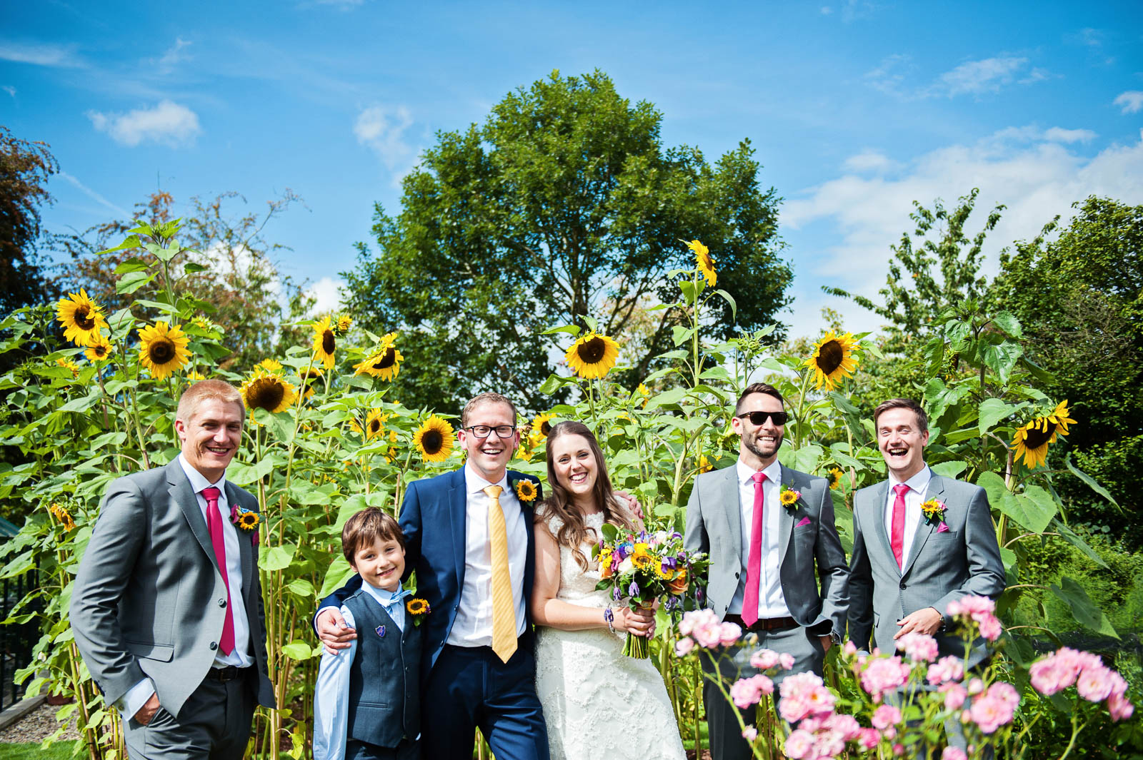 Bridal party having a group shot with sunflowers behind them.