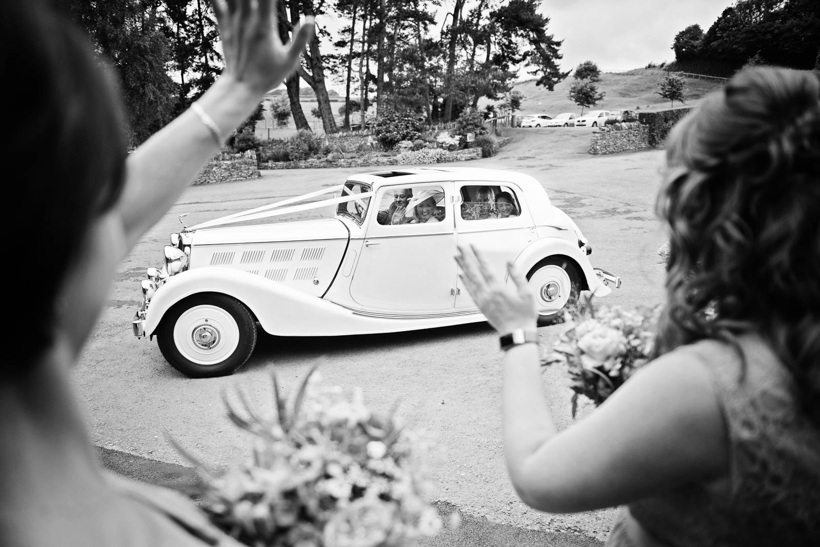Bridesmaids waving to the bride as she arrives with a classic car. 