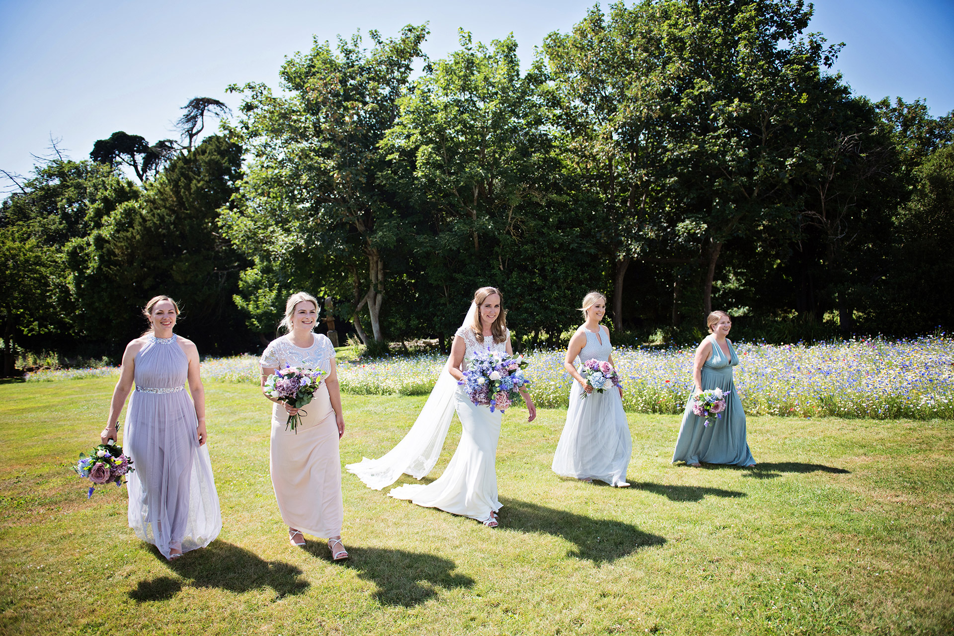 Bride with her bridesmaids walking together with a wildflower meadow behind them. Taken at Cleevdon Hall