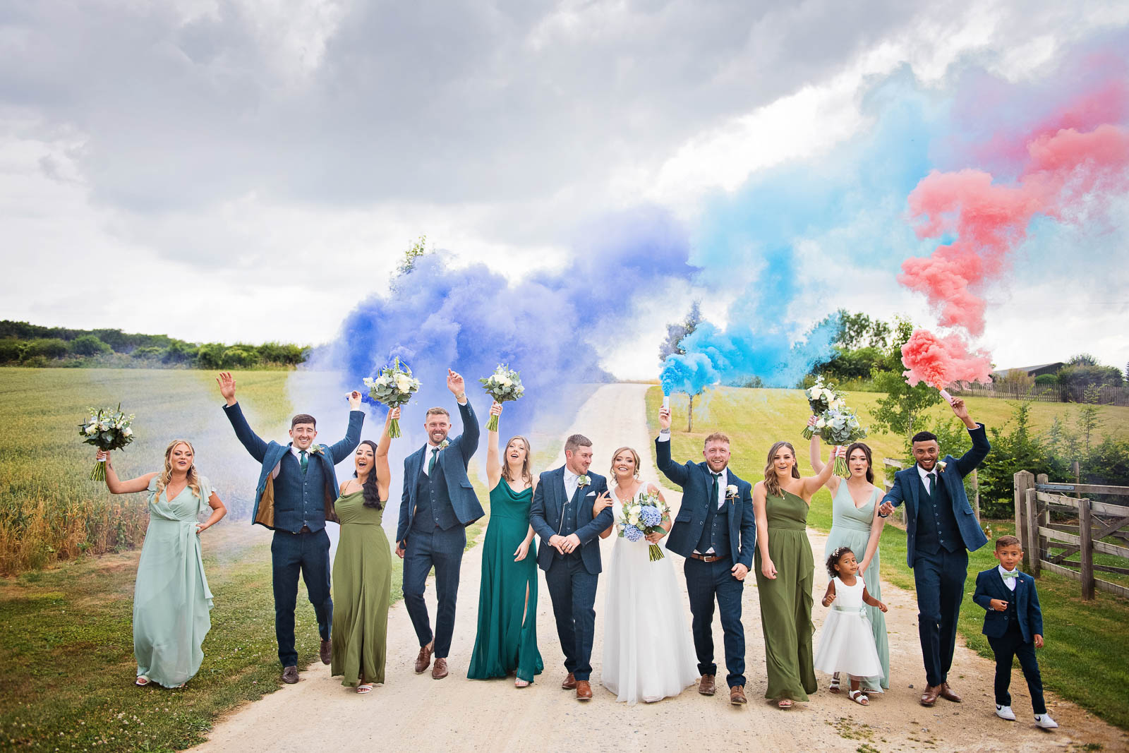 Bridal party walking in fields with coloured smoke bombs