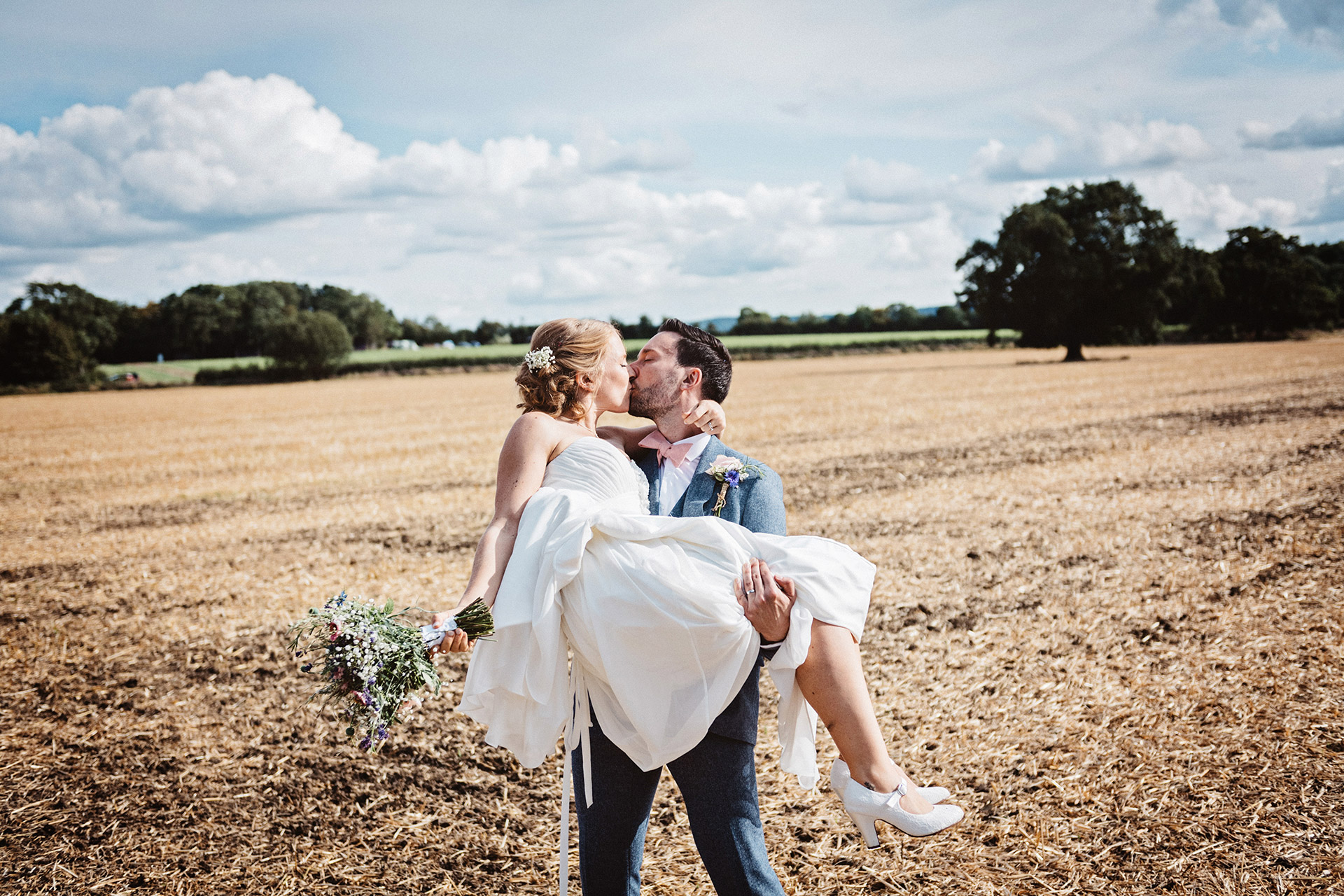 groom carry's bride in a harvested field in gloucestershire