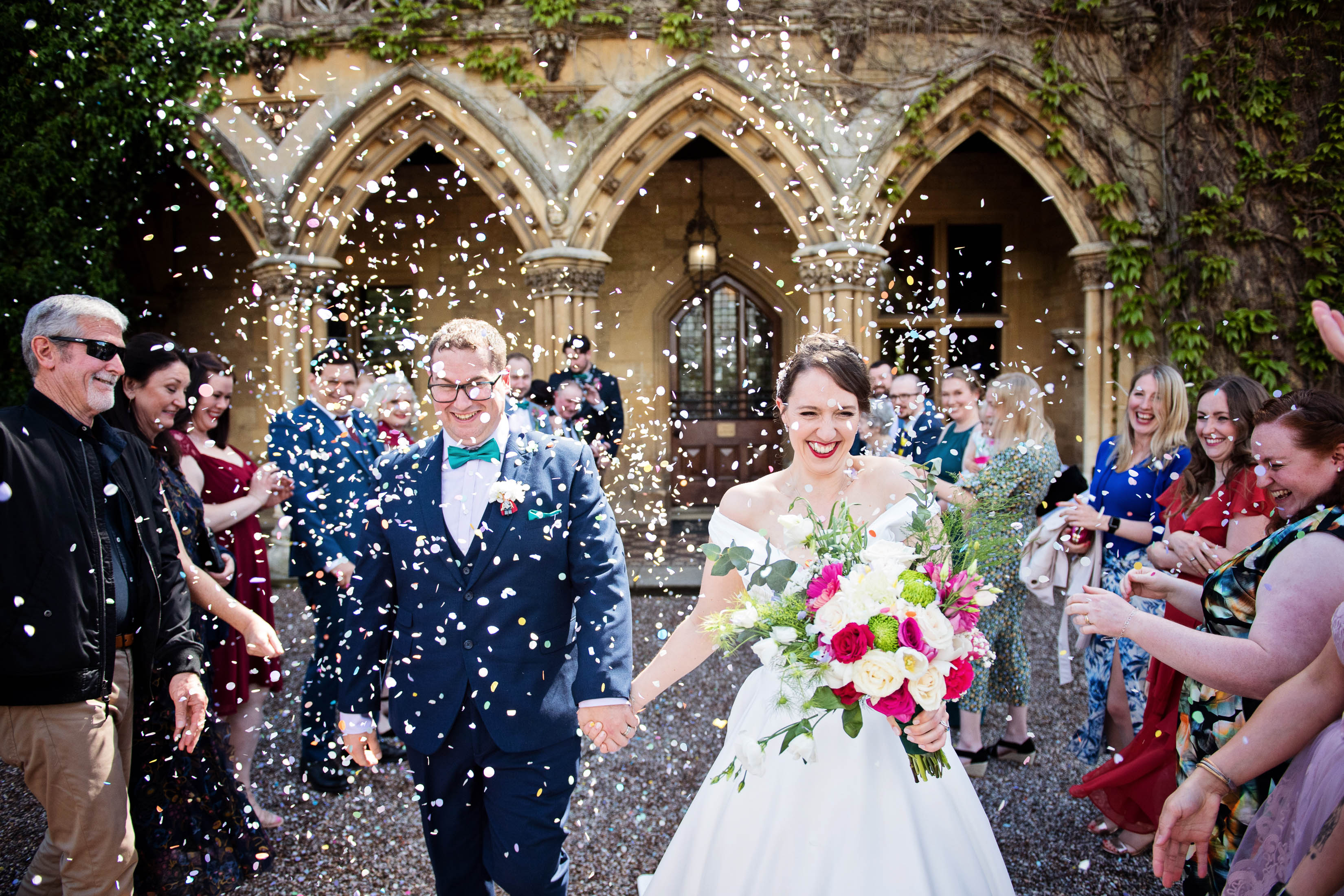 Bride and groom get showered in confetti by their wedding guests, with Manor By the Lake arches in the background. 