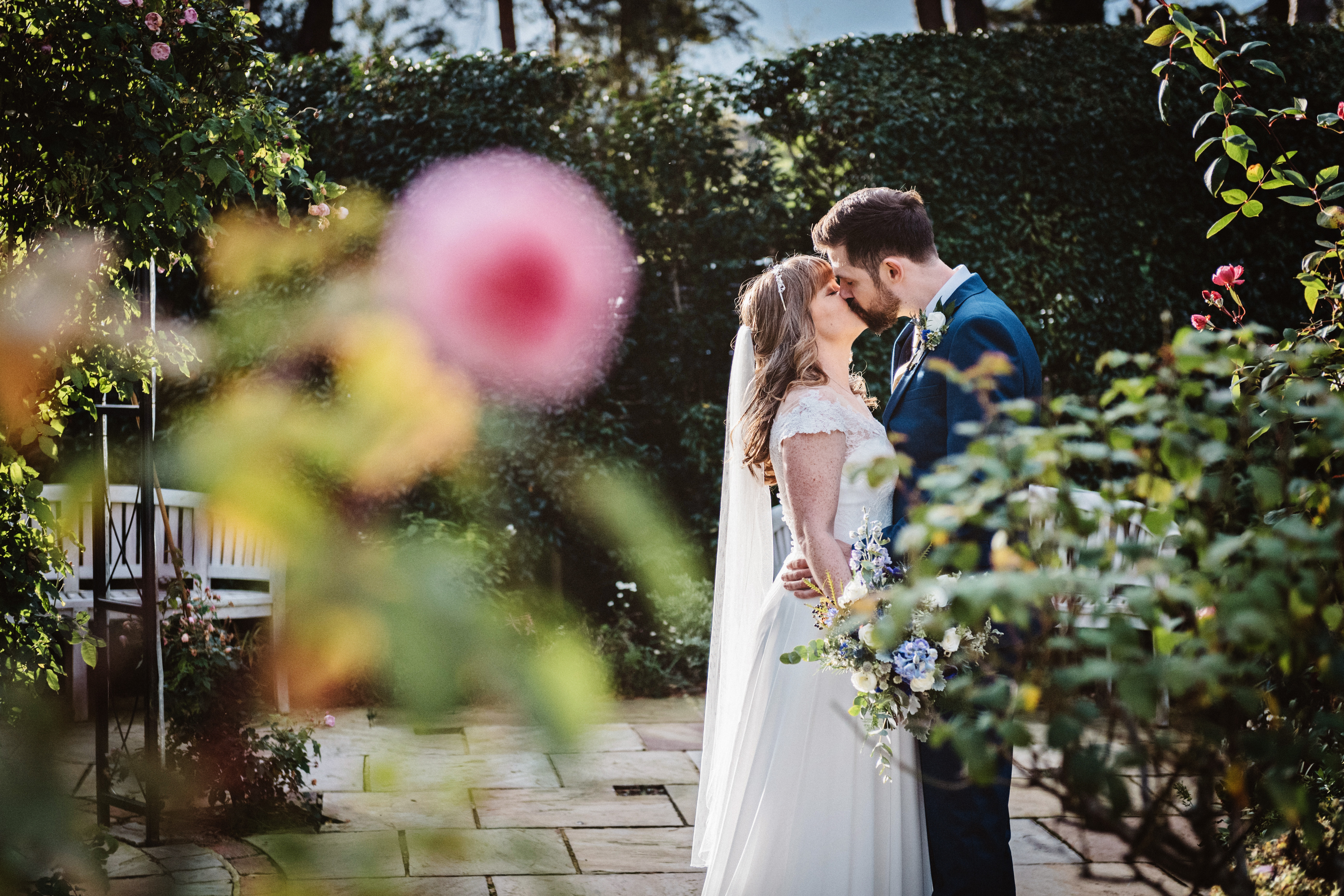 Bride and groom kiss in a gorgeous wedding garden with roses in front of them. Taken at The Kingscote Barn)