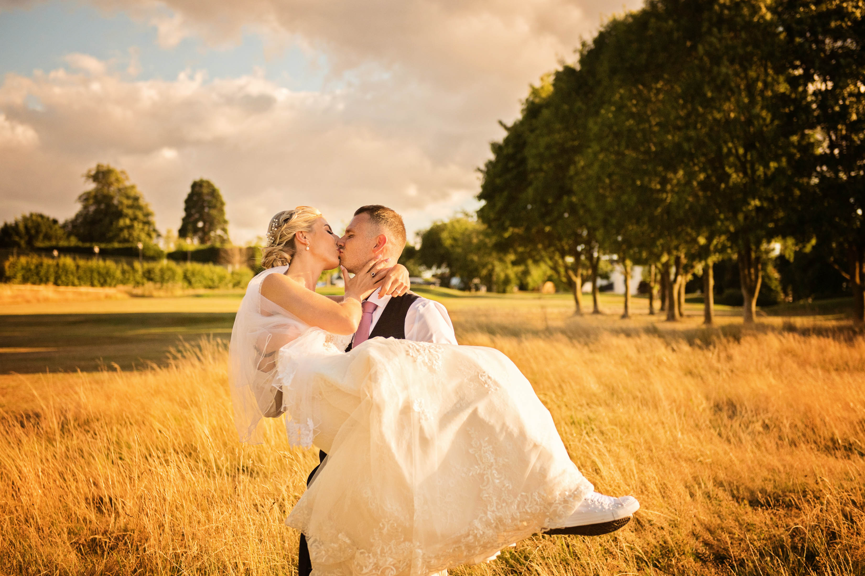 Groom carrying bride (whilst they kiss), during golden hour. 