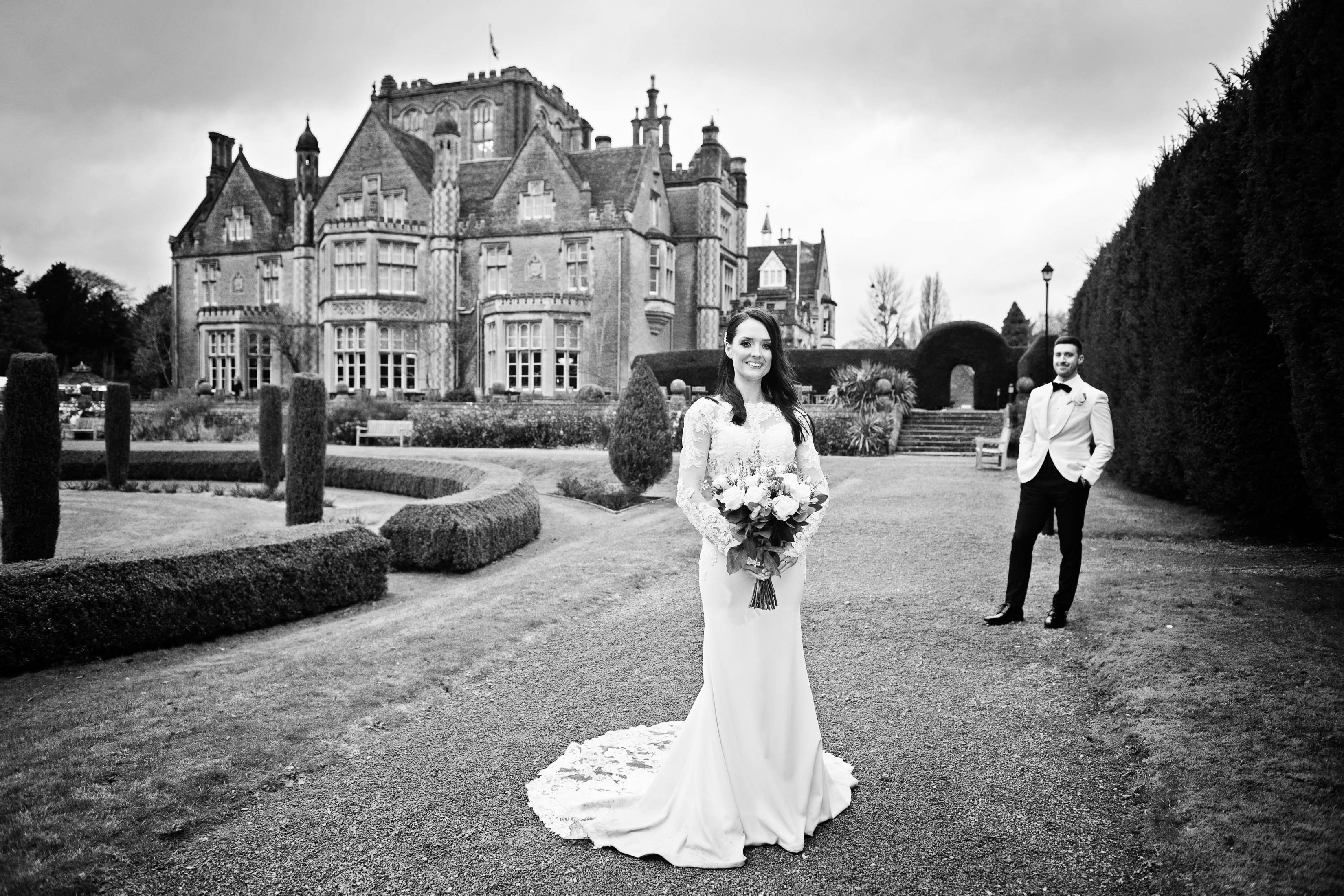 Black and white photo with bride standing in her gorgeous white dress, with her husband in the background along with Tortworth Court Hotel