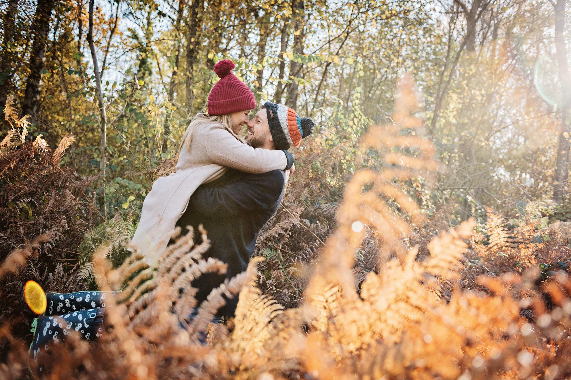 Couple lovingly embrace in amongst autumnal ferns and woodland with a stunning light crossing their path. 