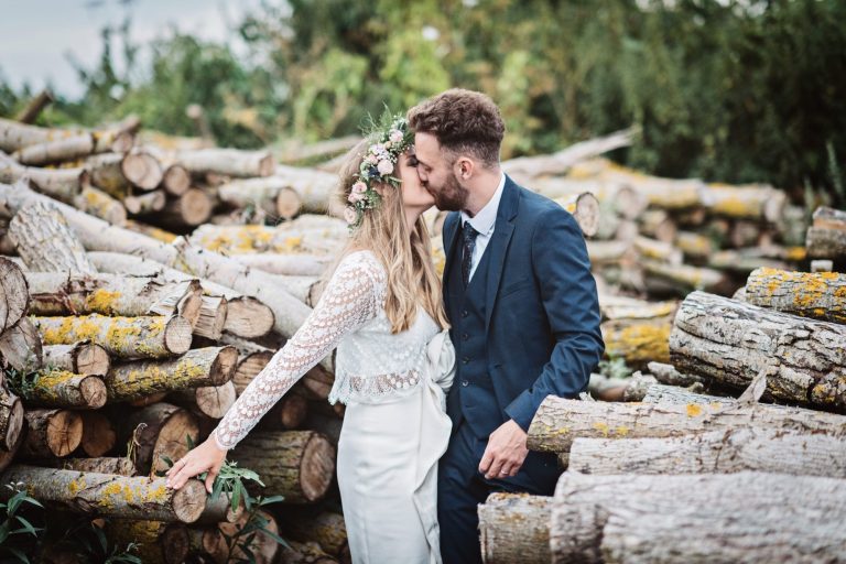 Dramatic photo of bride and groom kissing amongst a stack of logs. Photo by Blooming Photography