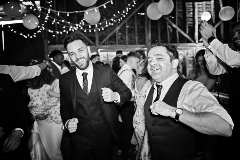 B&W fun photo of groom and his mate dancing like dads at a wedding at Over Barn, Gloucester. Photo by Blooming Photo