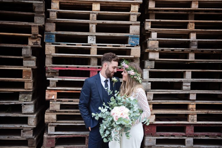 Bride & groom stand in front of wooden pallets. Sounds rubbish but actually half decent!