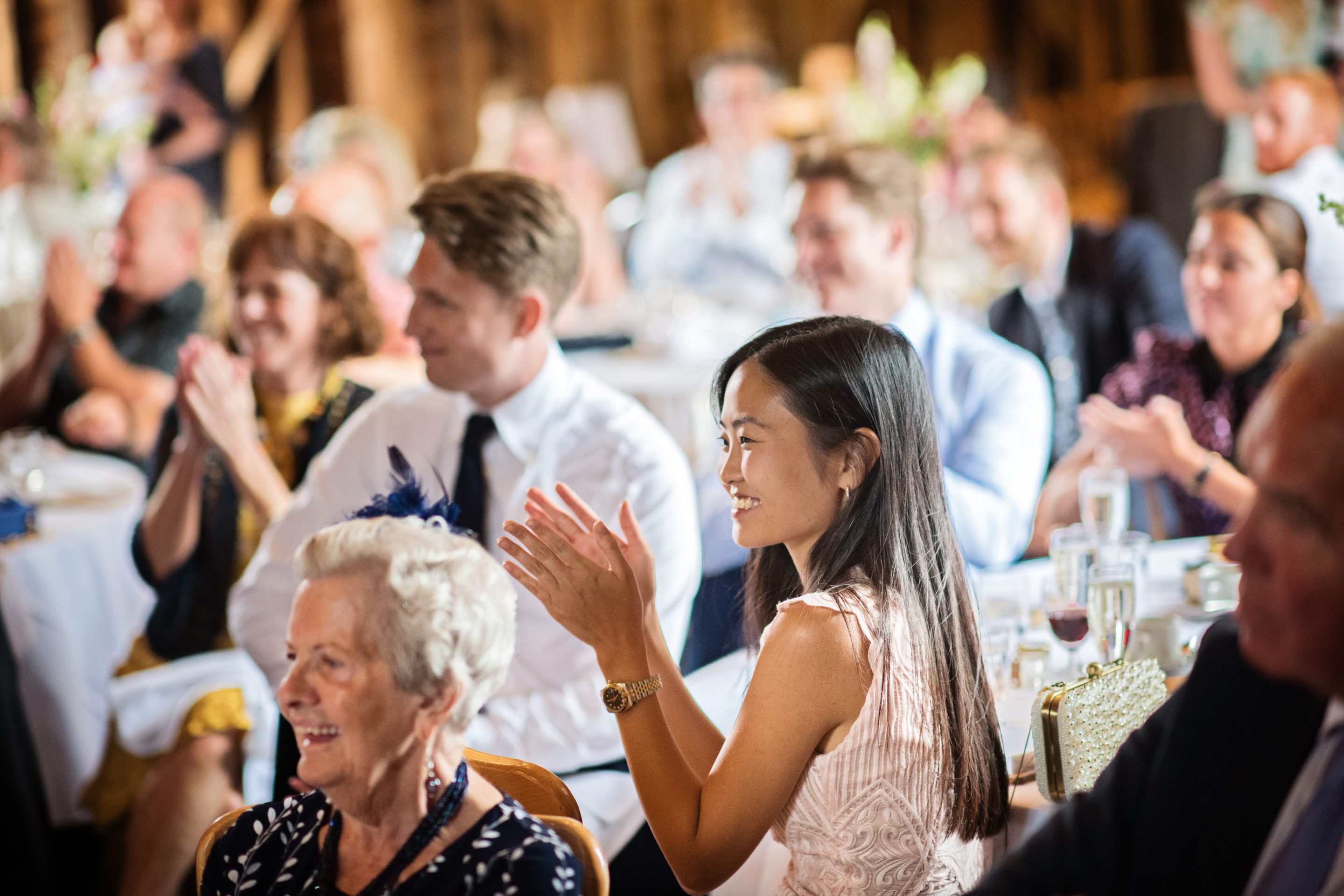 Candid photo of a wedding guest smiling at a wedding speech at Overbarn, Gloucester.