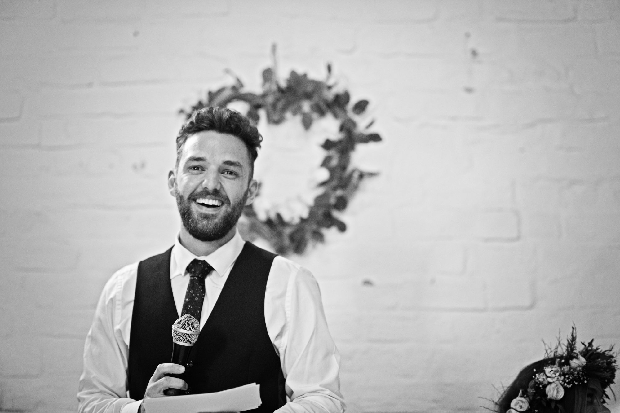 B&W photo of the groom doing his speech and looking at the camera candidly.