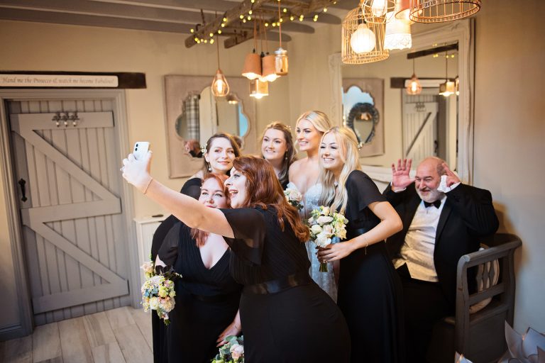 Bridesmaids and bride do a selfie just before the wedding. Father of the bride is pulling a funny face unbeknown to them! All in the bridal suite at Blackwell Grange.