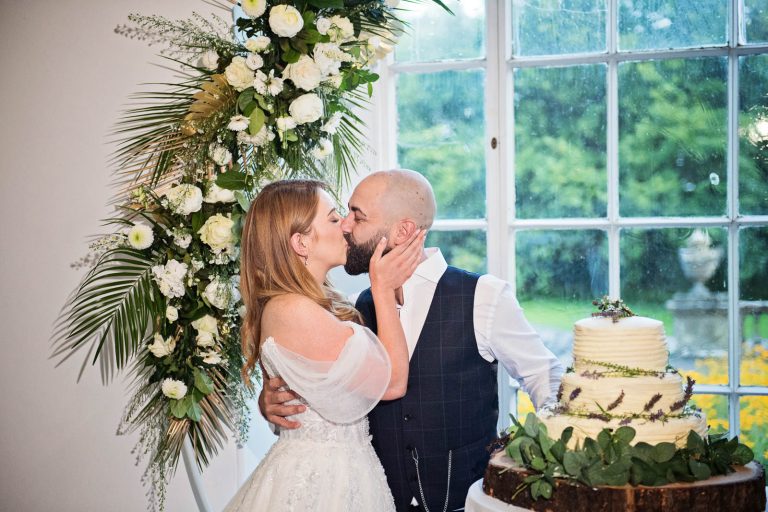 Photo of bride and groom kissing after cutting their wedding cake.