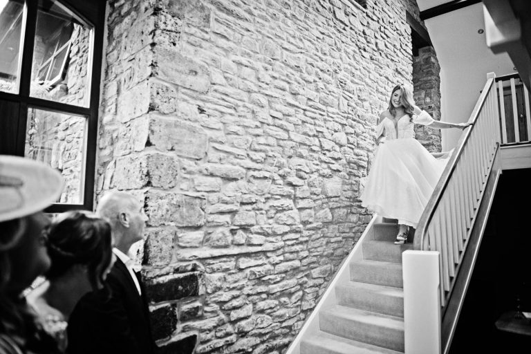 Natural photo of a bride walking down the stairs in her wedding dress as she see's her dad for the first time.