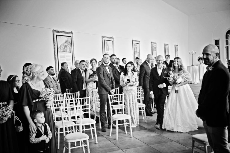 Relaxed B&W photo of a bride and her dad walking down the wedding isle.