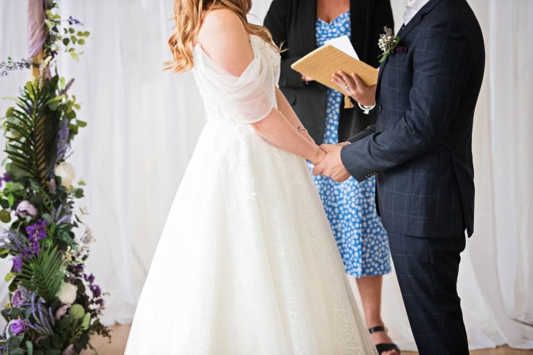 Photo of a bride and groom holding hands during the wedding ceremony at Margam Country Park.