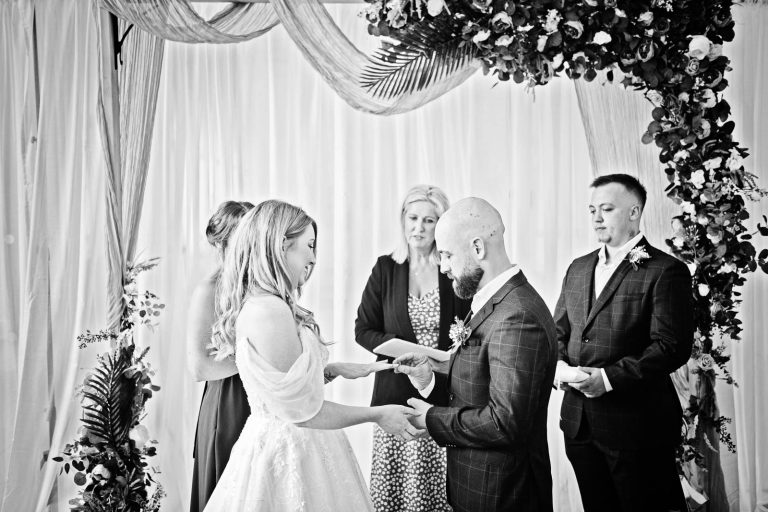 Black & white photo of a bride and groom exchanging rings.