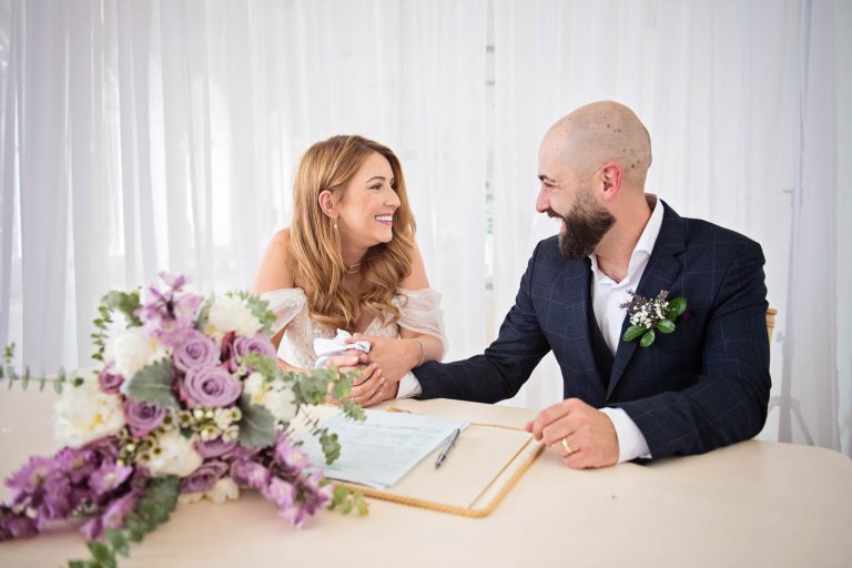 Bride and groom smiling at each other after signing the wedding register.