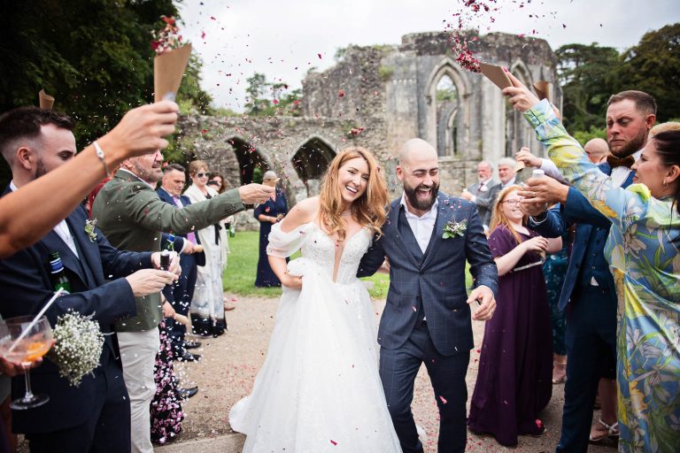Colour photo of a bride and groom smiling whilst having wedding confetti thrown at them.