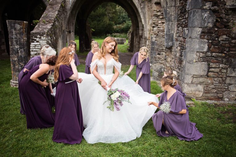 Bridesmaids gather the brides wedding dress with the ruins behind them.