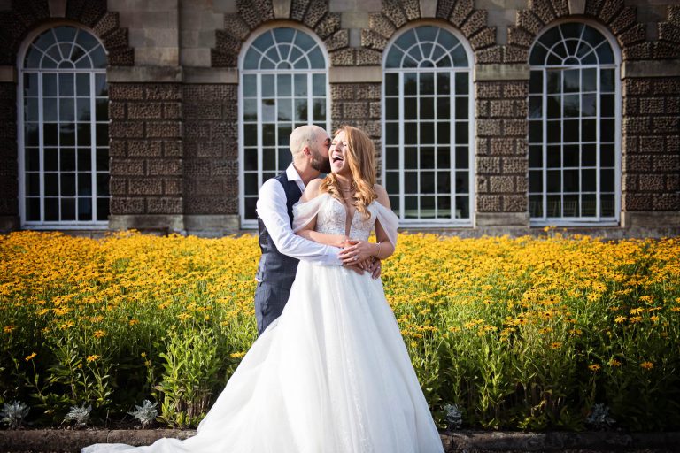 Natural wedding photograph of bride and groom hugging a laughing outside The Orangery.