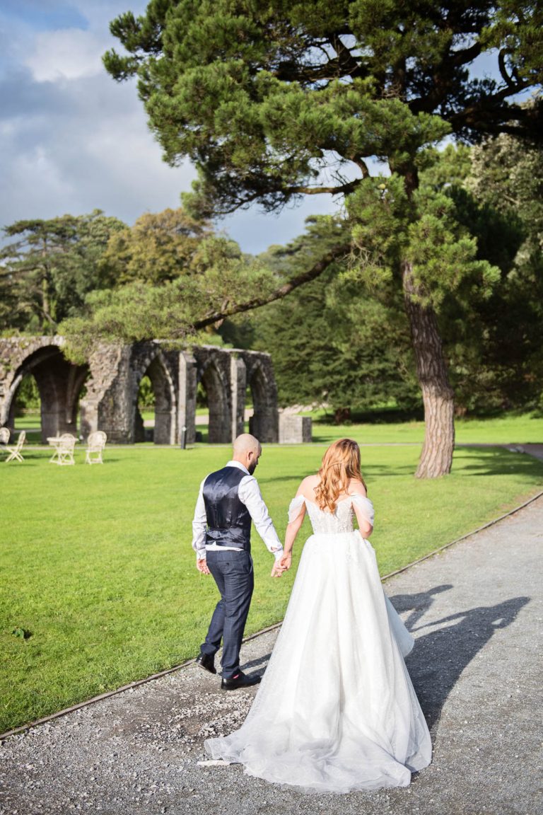 Natural wedding photography of bride and groom holding hands and walking away down a path.