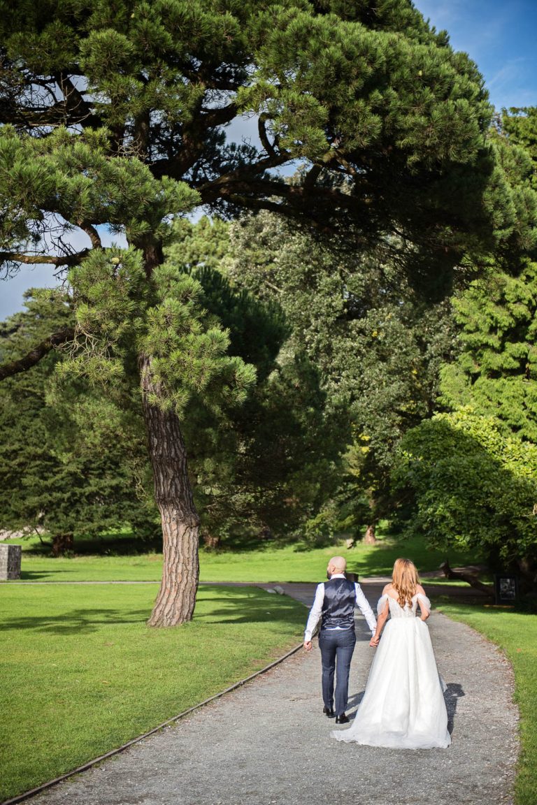 Relaxed wedding photography of bride and groom holding hands and walking away down a path.