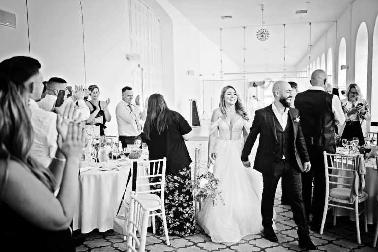 Natural image taken of the bride groom entering the wedding breakfast room cheered on by friends and family in The Orangery.