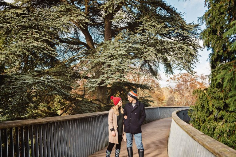 Couple walk along the treetop walkway at Westonbirt Arboretum for their engagement shoot.