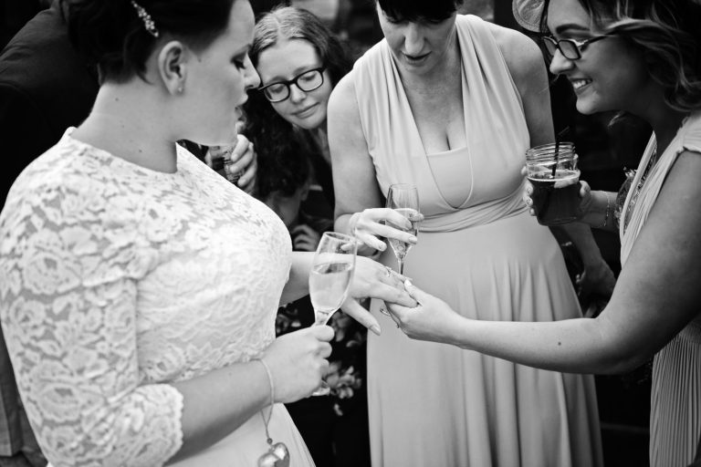 B&W candid photo of wedding guests looking at the brides wedding ring.
