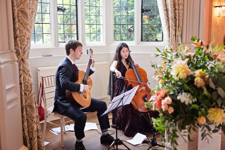 An acoustic guitarist and cello player playing emphatic music. A bouquet of flowers in the foreground.