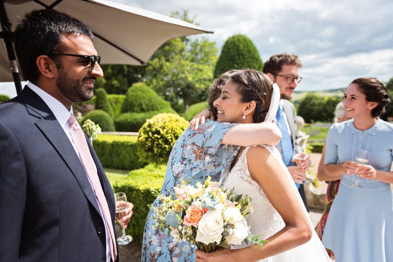 Candid photograph of the bride being hugged by a family member in the gardens of Danesfield House Hotel and Spa.