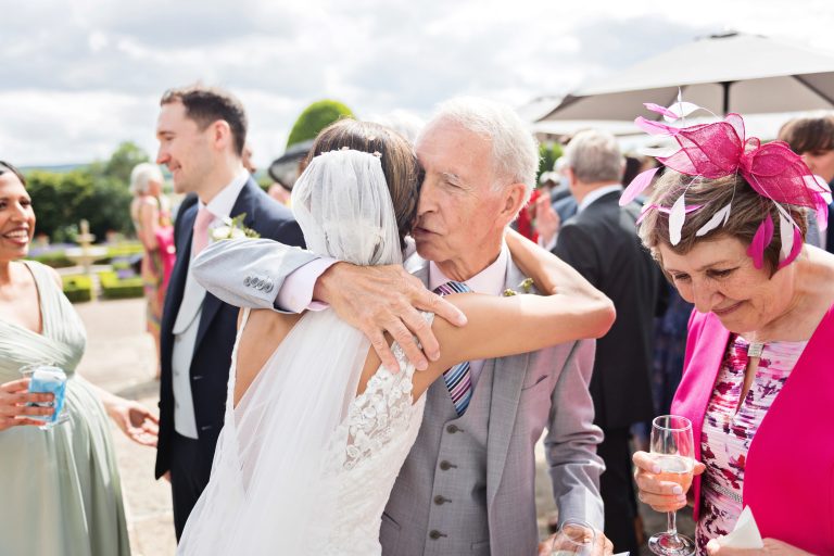 The father of the groom hugs the bride. Colourful photograph. Photographed at Danesfield House Hotel and Spa.