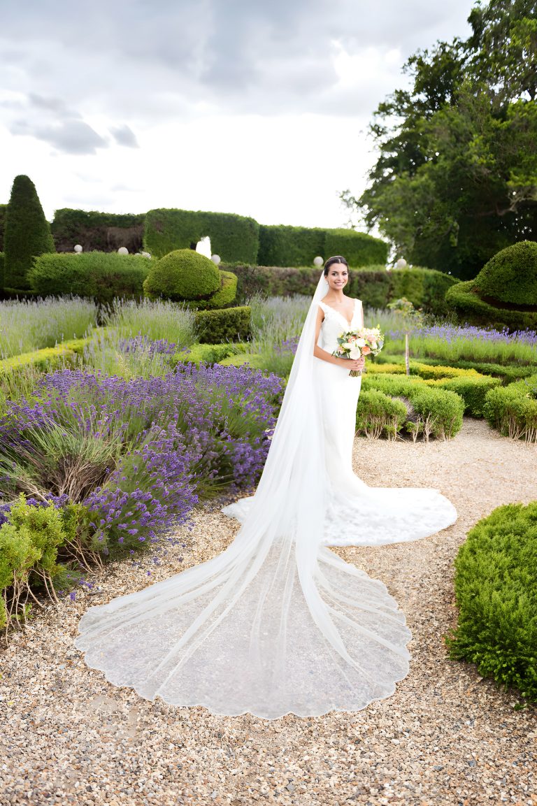 Portrait photograph of an elegant bride with her wedding veil and dress laid out. Lavender and formal gardens of Danesfield House Hotel and Spa in the background.