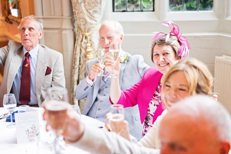 Guests including mother of the groom cheer to the grooms wedding speech. Photographed in Danesfield House Ballroom.