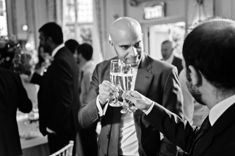 Guests "clink" their champagne glasses at the end of speeches. Black and white candid photo. Shot in the Danesfield House Ballroom.