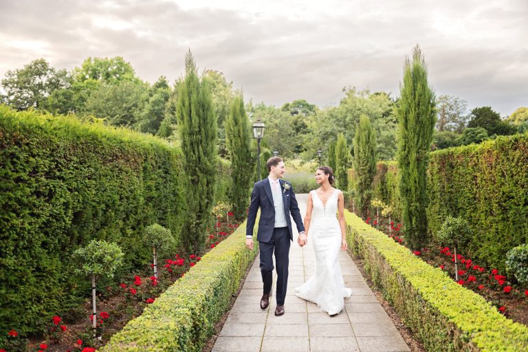 Bride and groom hand-in-hand walking down a paved path at Danesfield House Hotel & Spa wedding. Photography by Blooming Photography.