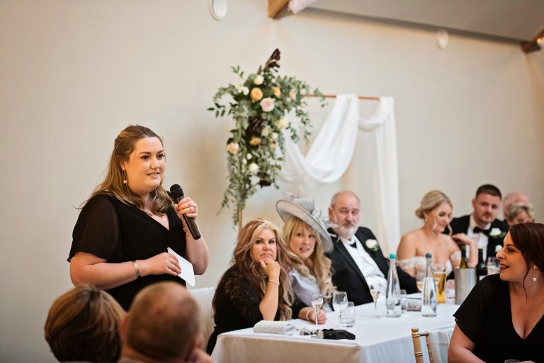 Maid of honour doing her speech. Top table including the bride is behind her. Candid photo by Blooming Photography. Taken at Blackwell Grange, Warwickshire.