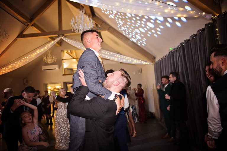 Image of a guest being held by another guest during a dance. Candid photo by Blooming Photography. Taken at Blackwell Grange, Warwickshire.