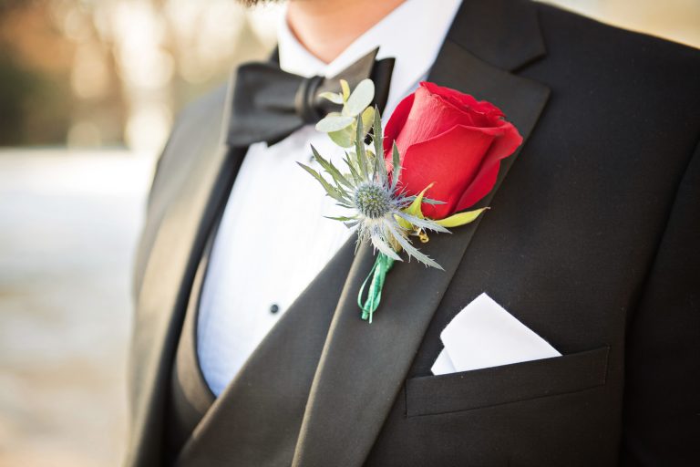 A close up of a grooms button hole, (red rose and spiky Eryngium planum). Photographed by Blooming Photography at Eastington Park