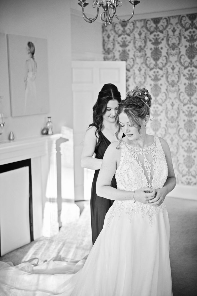 B&W portrait photo of bride having her wedding dress done up taken at Eastington Park winter Wedding, by Blooming Photography
