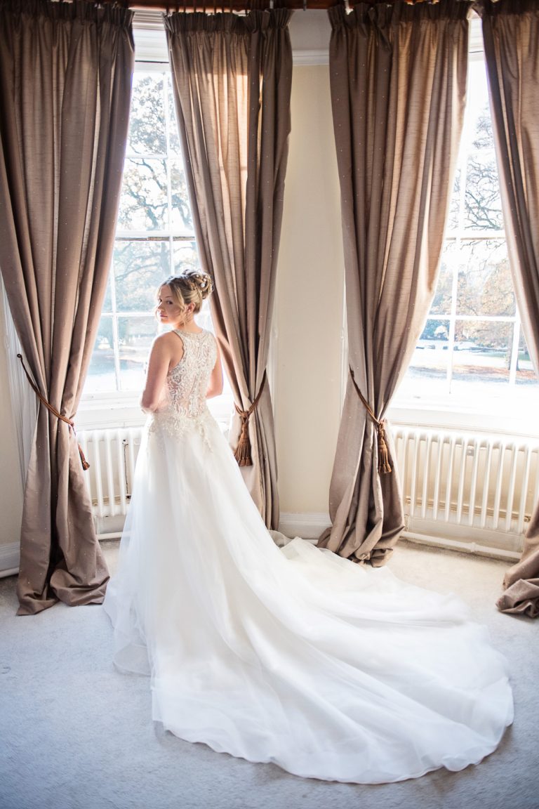 Elegant photo of bride in her wedding dress standing up at the large Georgian bay window at Eastington Park