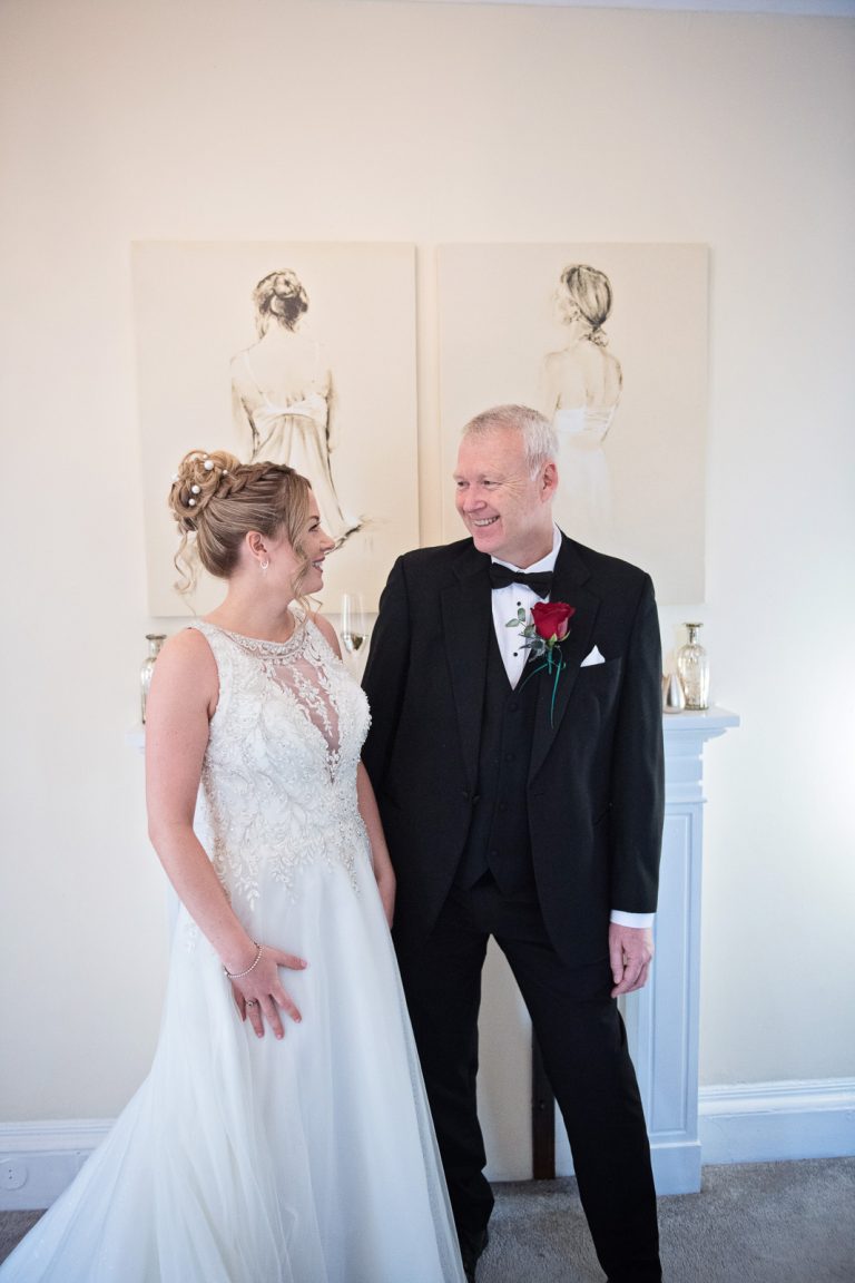 Bride and brides father looking and smiling at each other (natural). Taken at Eastington Park by Blooming Photography.