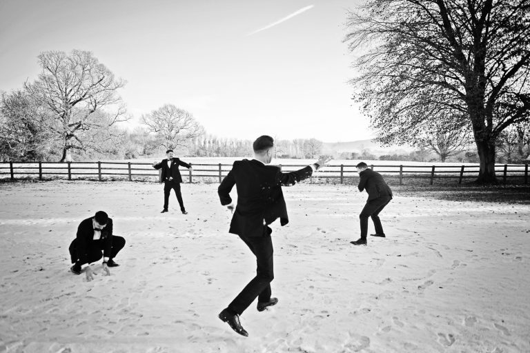 B&W photo of groomsmen having a snowball fight in the grounds of Eastington Park, Gloucestershire.
