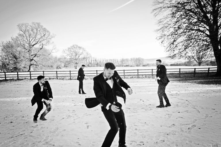 B&W photo of groomsmen having a snowball fight in the grounds of Eastington Park, Gloucestershire.